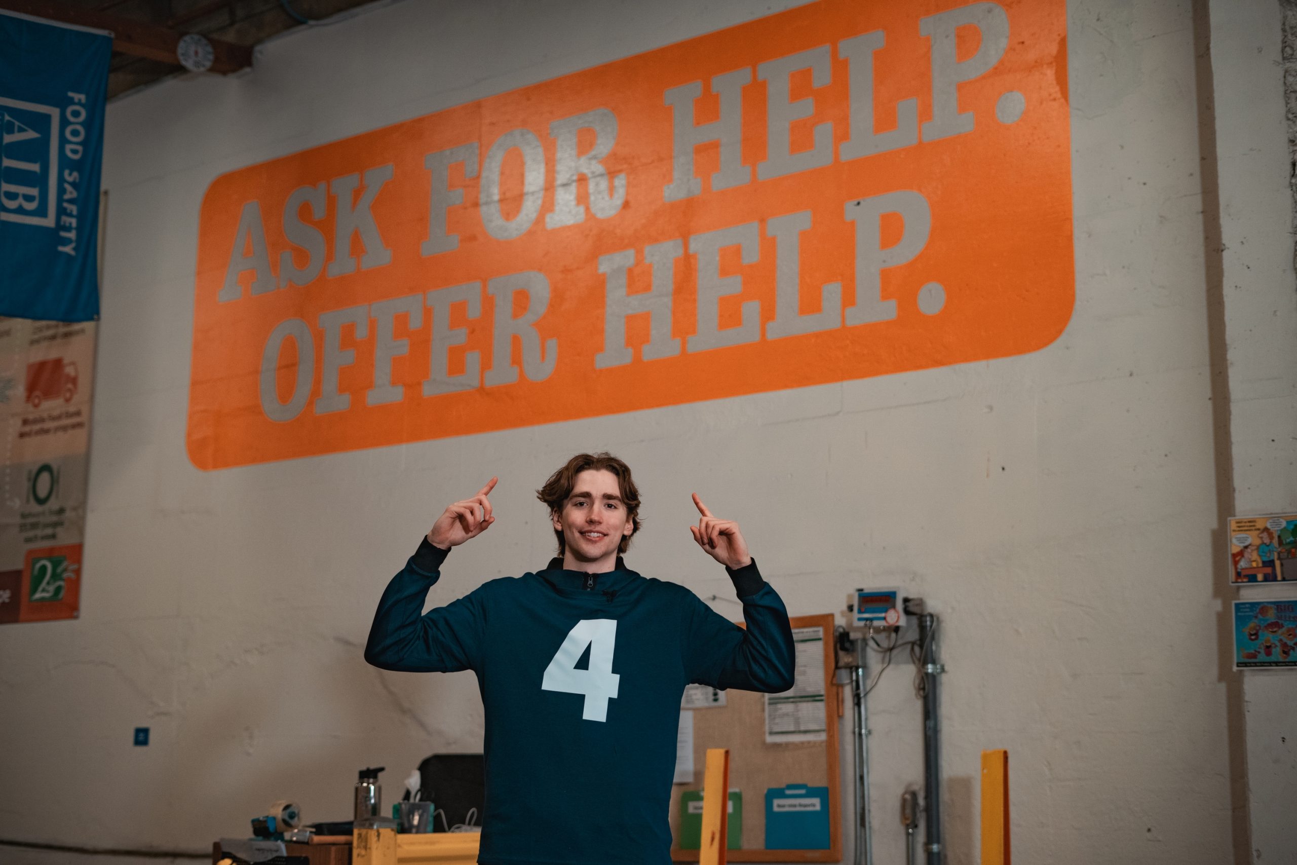 Dusty Stromer, Gonzaga basketball player, poses in the Second Harvest Warehouse in front of a mural reading, "Ask for help. Offer help."